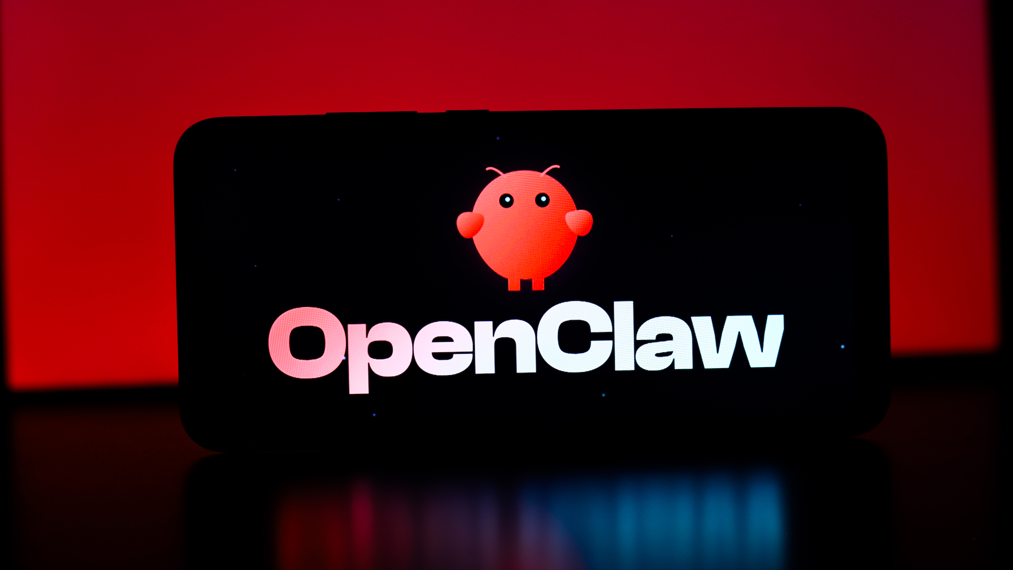 OpenClaw AI logo displayed on a smartphone screen against a red background, illustrating a blog discussion about emerging open-source AI platforms and their competitive impact.